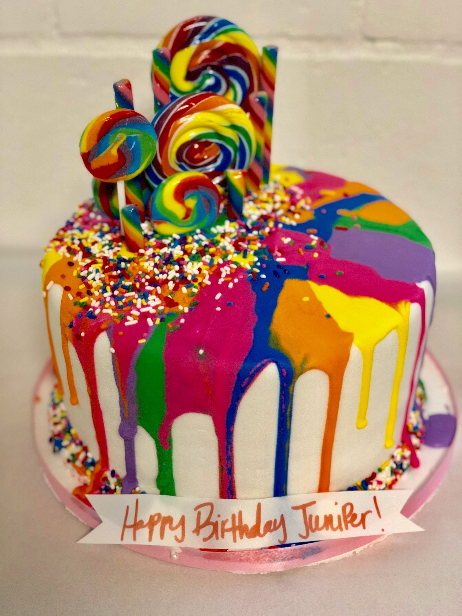 Rainbow drip cake with sprinkles and lollipops on white buttercream